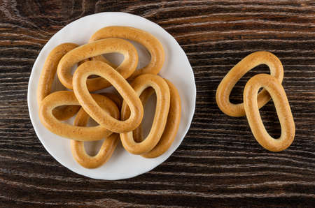 Oval bread rings in white glass plate, two baranka on dark wooden table. Top view