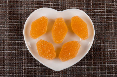 Orange color marmalades in heart shape plate on dark mat. Top view