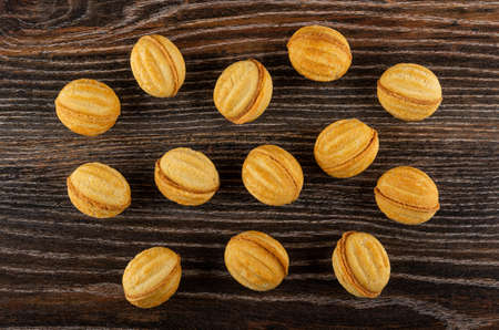 Background from scattered cookies in nut shape with filling on dark wooden table. Top view