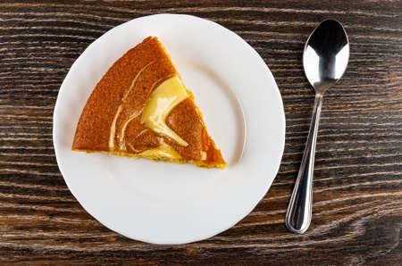 Slice of Ñake with cream and jam in white plate, teaspoon on dark wooden table. Top viewの写真素材