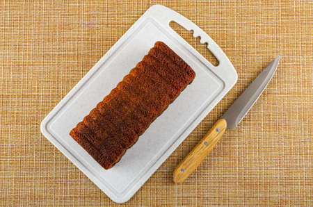 Baked muffin on plastic cutting board, kitchen knife on brown mat. Top view
