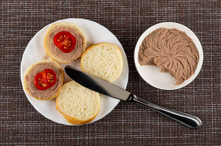 Sandwiches from wheat bread, liver pate and tomato in white plate, table knife, bowl with liver pate...