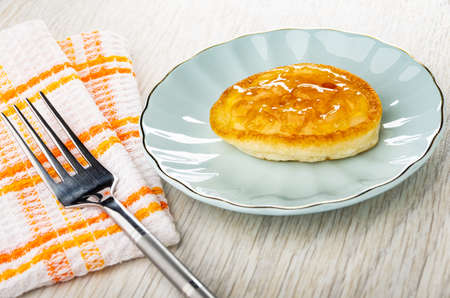 Fork on checkered napkin, homemade small pancake with lemon jam in blue saucer on wooden table