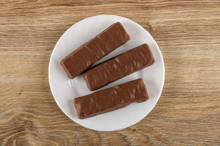 Three chocolate bar with filling in white glass plate on wooden table. Top view