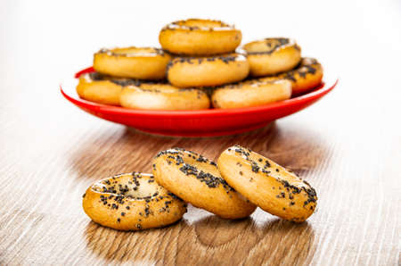 Bread rings with poppy seeds in red saucer on background, three bread rings on brown wooden tableの写真素材