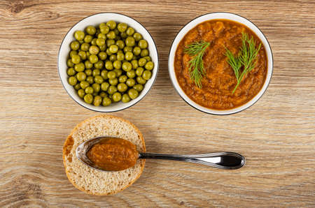 Green peas in bowl, squash caviar with dill in white bowl, vegetable caviar in spoon on slice of bun on wooden table. Top viewの写真素材