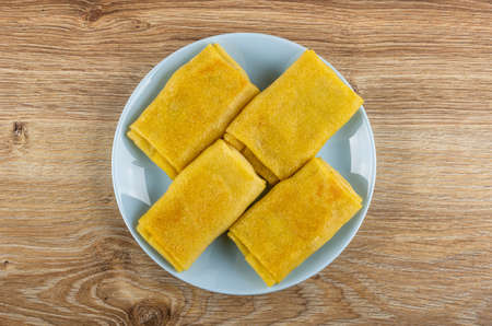 Few pancake rolls with filling in blue plate on brown wooden table. Top view