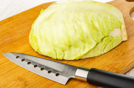 Half head of white cabbage and kitchen knife on cutting board on wooden tableの写真素材