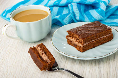 Striped napkin, coffee with milk in cup, small chocolate cake in blue saucer, piece of cake in...