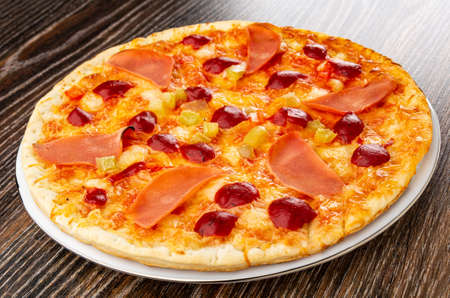 Baked pizza with sausage in white glass plate on dark wooden tableの写真素材