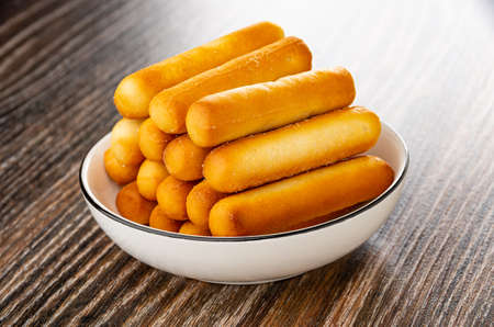 Small bread sticks in white glass bowl on dark wooden tableの写真素材