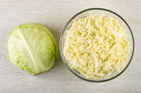 Half head of cabbage, transparent glass bowl with chopped white cabbage on wooden table. Top viewの写真素材