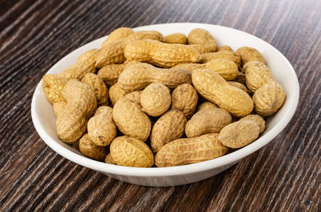 Fried peanuts in peel in glass bowl on dark wooden table