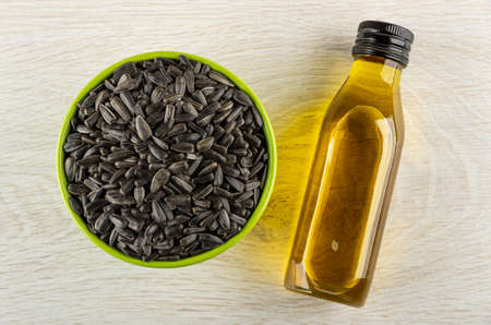 Fried unpeeled sunflower seeds in green bowl, transparent bottle with sunflower oil on wooden table. Top viewの写真素材