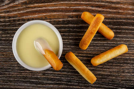 Small bread stick dipped in condensed milk, few breadsticks on dark wooden table. Top viewの写真素材