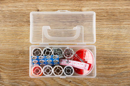 Sewing kit in opened transparent plastic box on wooden table. Top view