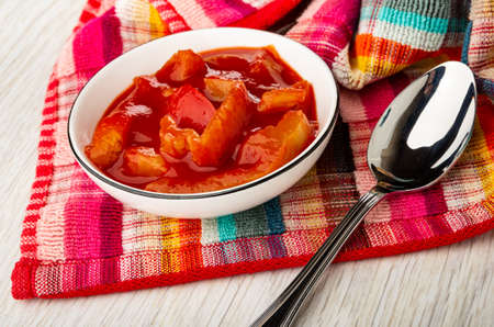 White glass bowl with lecho, spoon on checkered napkin on wooden tableの写真素材