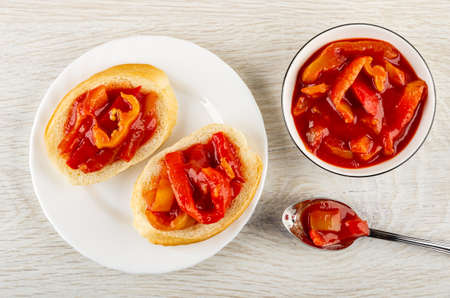 Two sandwiches from wheat bread with lecho in white glass plate, bowl and spoon with lecho on wooden table. Top viewの写真素材