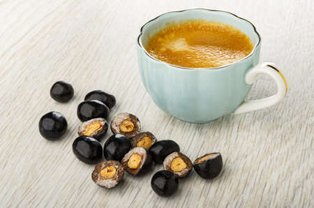 Chocolate dragee with peanut, halves of dragee, blue cup with black coffee on wooden table