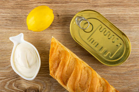 Fresh yellow lemon, bowl with mayonnaise, wheat baguette, closed jar with canned fish on wooden table. Top viewの写真素材