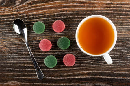 Teaspoon, red and green marmalades, cup with hot tea on dark wooden table. Top viewの写真素材