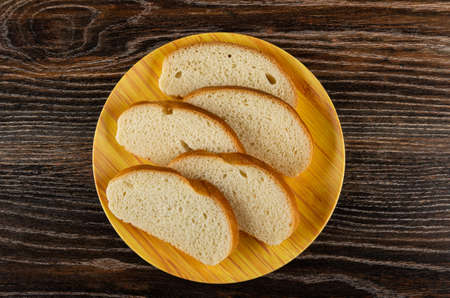 Slices of wheat bread in brown plate on dark wooden table. Top view