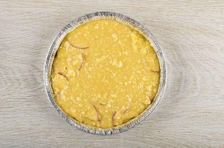 Raw dough from cottage cheese with slices of apple in aluminium mold on wooden table. Top viewの写真素材