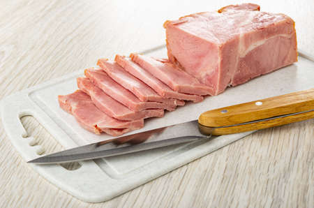 Slices of pressed bacon, kitchen knife on plastic cutting board on wooden table