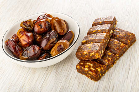 Dates in white glass bowl, energy bars with dates, orange and peanut on wooden tableの写真素材