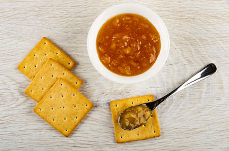 Few dry cookies, bowl with lemon jam, teaspoon with jam on cracker on wooden table. Top viewの写真素材