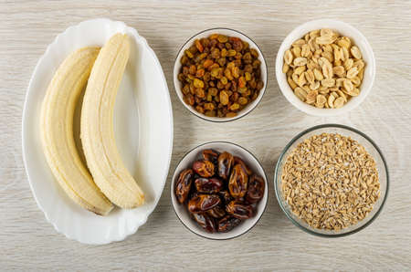Peeled banana in plate, raisin, peanut, dates and oat flakes - ingredients for cooking muesli cookies on wooden table. Top viewの写真素材