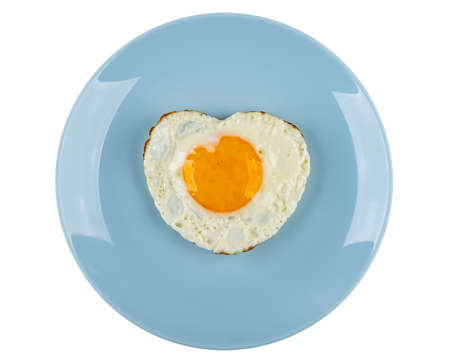 Fried egg in heart shape on blue plate isolated on white background. Top viewの写真素材