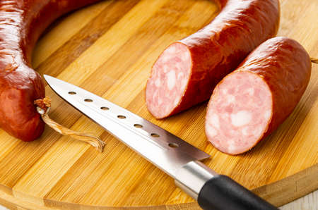 Section of smoked sausage ring, kitchen knife on striped bamboo cutting boardの写真素材