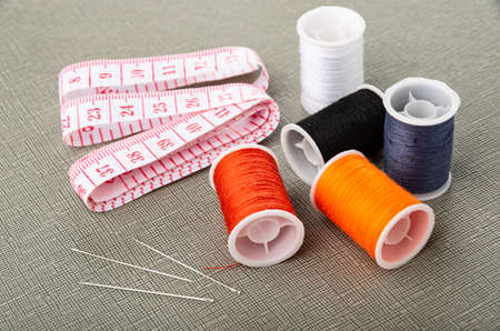 Measure tape,  spool with sewing threads of different color, sewing needles on gray table