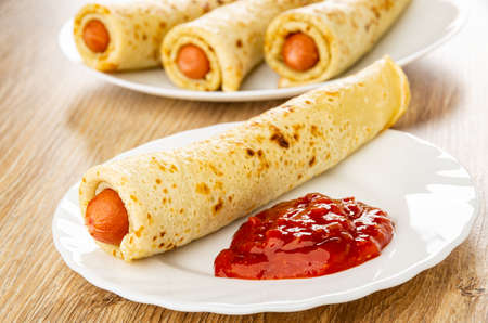 Three pancake rolls with sausages, pancake roll in plate with ketchup on wooden tableの写真素材