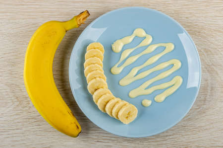 Unpeeled banana, slices of banana, sweet condensed milk in blue plate on wooden table. Top viewの写真素材