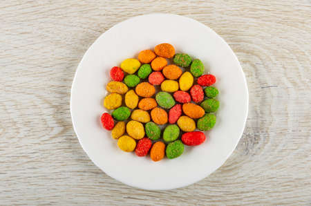 Multicolor salted dragee with peanut in white glass plate on wooden table. Top view