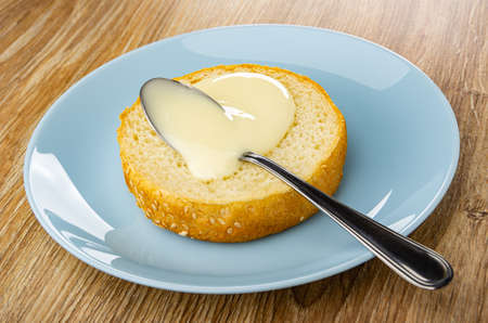 Teaspoon with condensed milk on half of bun in blue glass plate on wooden table