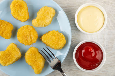 Fork on glass blue plate with fried chicken nuggets, white bowls with ketchup and mayonnaise on...