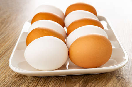 White and brown chicken eggs in glass plate on wooden table