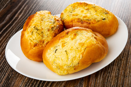 Three buns with cheese and garlic in white plate on dark wooden table
