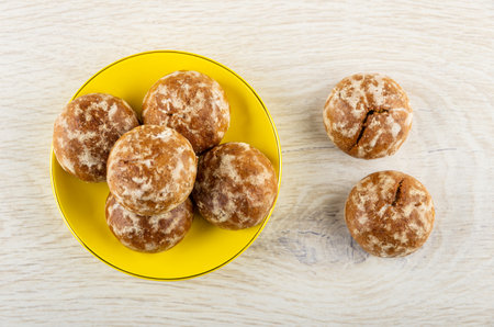 Small gingerbread cookies in yellow saucer, two cookies on wooden table. Top view