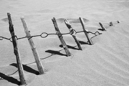 Rusty Fence almost buried in the sand on a sunny day. Black and white.の写真素材