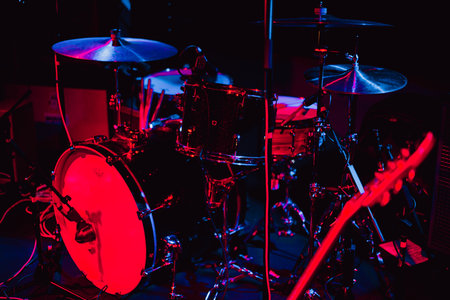 Drum kit and an electric guitar on stage under red, blue and purple neon glow stage lights of club, ready for the showの写真素材