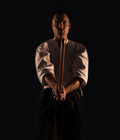 Aikido practicer (Aikidoka) with a training wooden sword (boken) dark dojo photoの写真素材