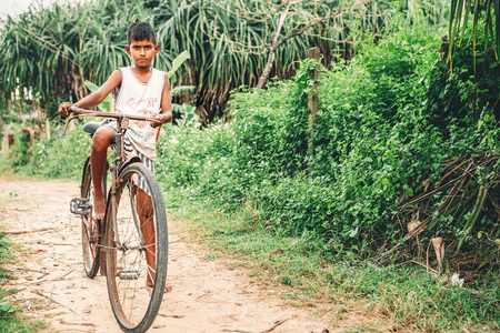 Weligama, Sri Lanka - December 21 , 2017: Little barefoot boy stands near the old rusty bicycle and poses for a photo in Weligama, Sri Lankaのeditorial素材