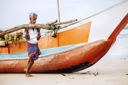 Weligama, Sri Lanka  December 21, 2017: Old fisherman pushing the fishing boat out the water portrait in Weligama, Sri Lankaのeditorial素材