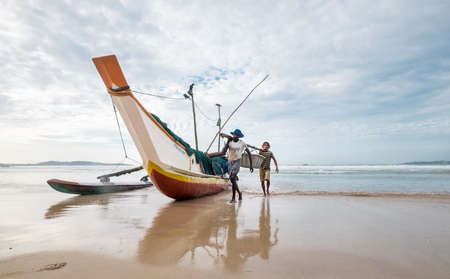 Weligama, Sri Lanka December 21, 2017: Two Fishermen floating on the boat returning home after the night fishing in the morning time. They carrying catch together a  in Weligama, Sri Lanka.のeditorial素材