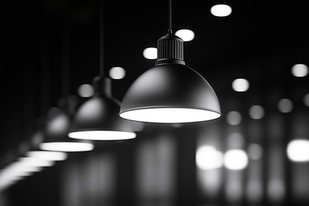 Black-and-white photo of industrial-style pendant lights with ribbed metallic details, casting a subtle glow in a dark interior. Shot from a side angle, emphasizing sleek, modern design and texture.の素材