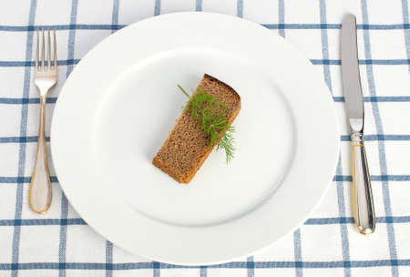 Piece of bread and dill on the plate with fork and knife on tablecloth